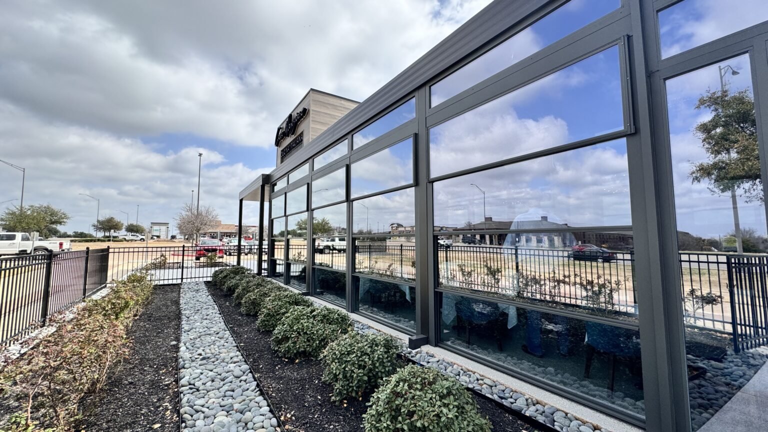 Dark aluminum pergola frame and glass walls along the restaurant patio